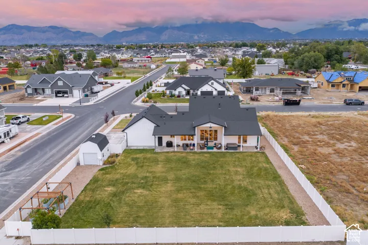 Aerial perspective featuring an expansive fenced backyard, detached storage shed, covered patio, and mountain backdrop