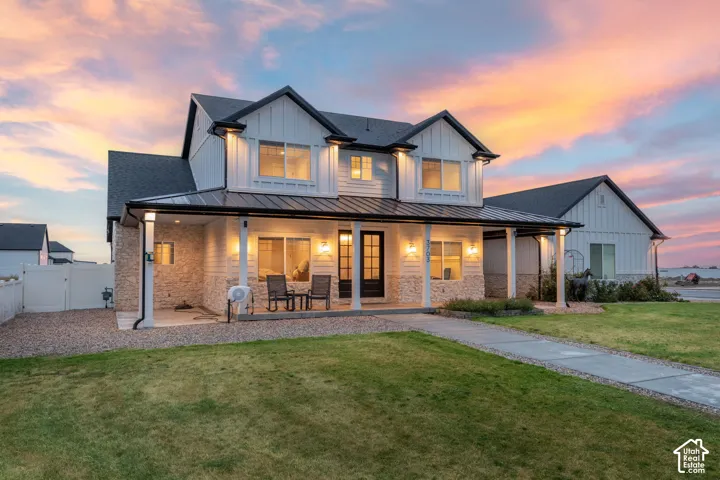 Two-story farmhouse-style exterior featuring vertical board-and-batten siding, stone accents, a covered front porch with metal roofing, and a concrete walkway