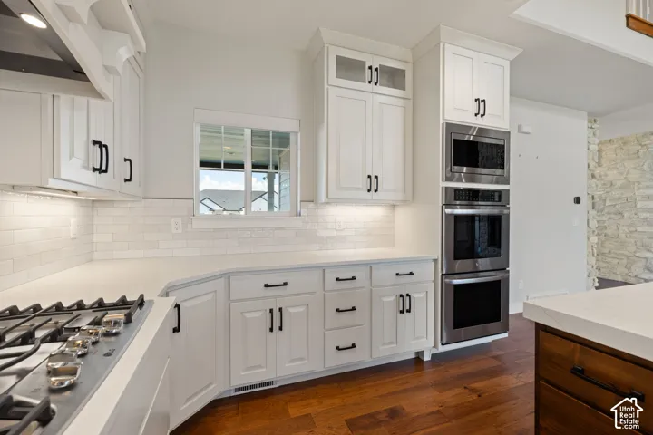Kitchen featuring white cabinetry with glass-front uppers, light quartz countertops, a subway tile backsplash, built-in stainless steel double ovens, and hardwood flooring