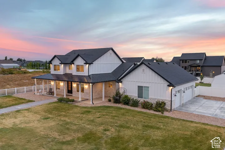 Two-story exterior featuring white vertical siding, stone masonry accents, a metal-roofed covered porch, and a multi-car garage