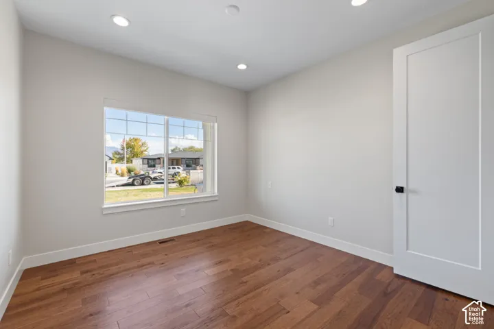Main floor bedroom featuring hardwood flooring, recessed lighting, a single-panel interior door with matte black hardware, and a window with a mountain backdrop