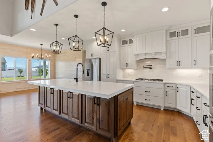 Kitchen featuring an expansive island with a light quartz countertop, dual-tone cabinetry, hardwood flooring, lantern-style pendant lighting, and a brick-patterned tile backsplash