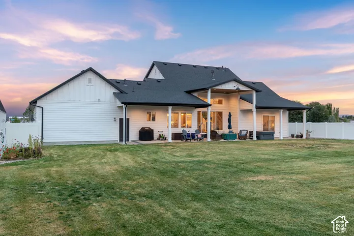Rear exterior featuring white horizontal siding, a covered patio with support columns, asphalt shingle roofing, and a privacy-fenced backyard