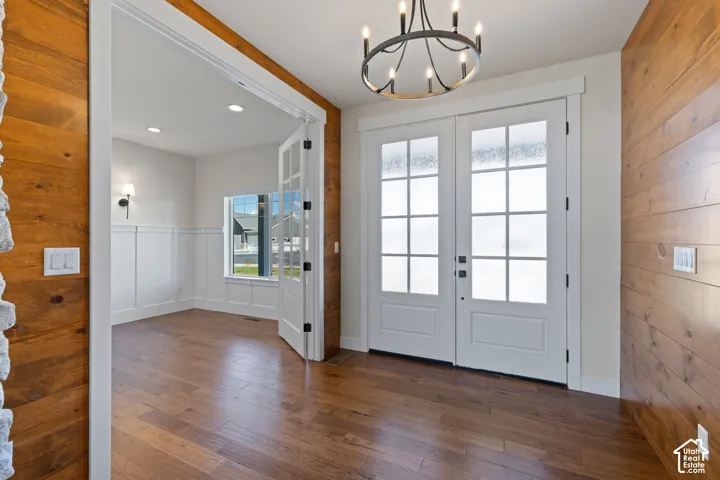 Entryway featuring horizontal wood-plank wall paneling, hardwood flooring, dual French glass-panel doors, and a circular multi-arm chandelier