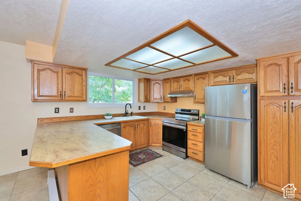 Kitchen featuring wood cabinetry, stainless steel appliances, tile flooring, recessed ceiling lighting, and a peninsula countertop