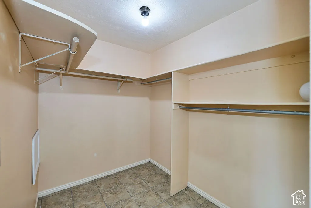 Walk-in closet featuring stone-finish tile flooring, multi-level fixed shelving, integrated garment rods, and overhead lighting