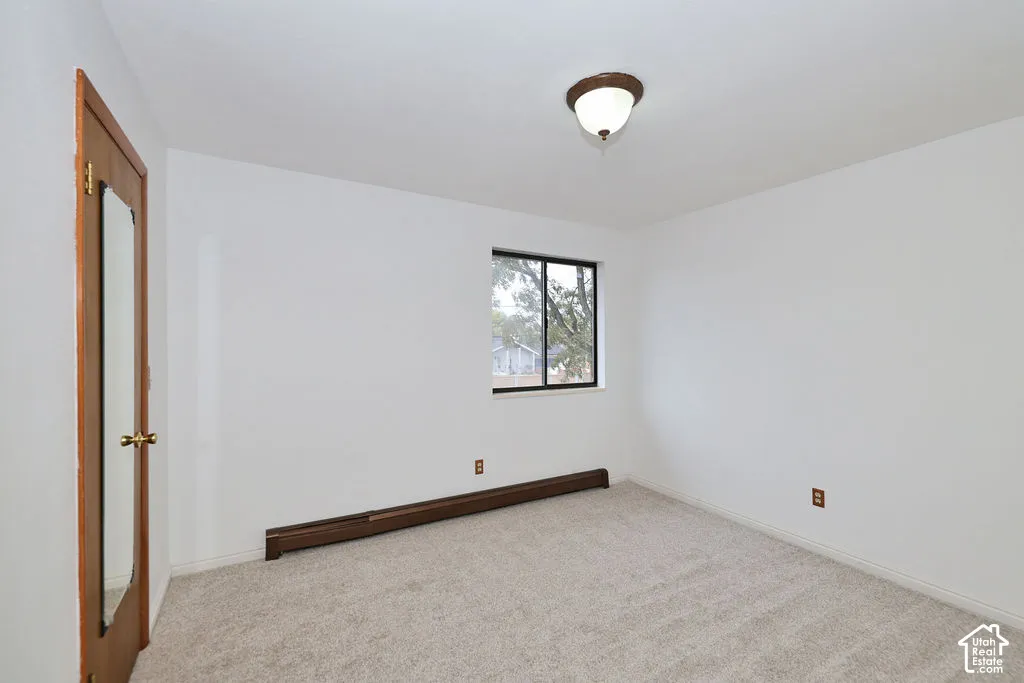 Neutral-toned wall-to-wall carpeting, wood-finish interior door, dual-pane window, flush-mount ceiling light fixture, and horizontal heating element