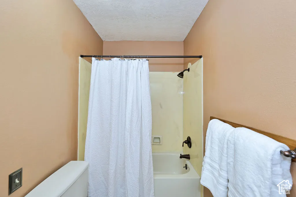 Tub and shower combination with light-toned surround, dark-finish plumbing fixtures, and wall-mounted towel rack
