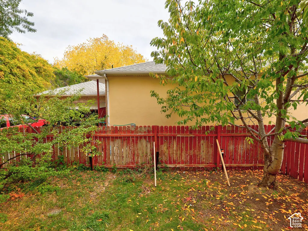 Rear exterior featuring a solid-color stucco facade, mature trees, and a wooden perimeter fence