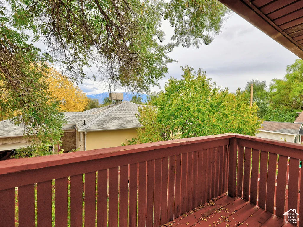 Elevated outdoor deck with wooden railing featuring mature trees and mountain scenery
