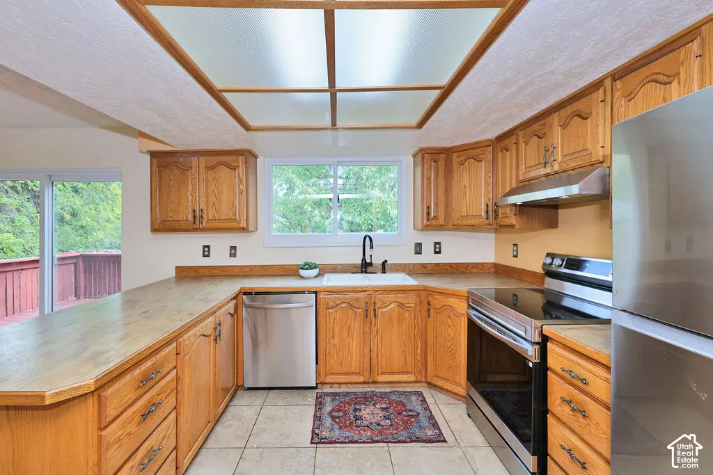 Kitchen featuring wood cabinetry, stainless steel appliances, tile flooring, a dual-basin sink with a matte black faucet, and a recessed ceiling panel