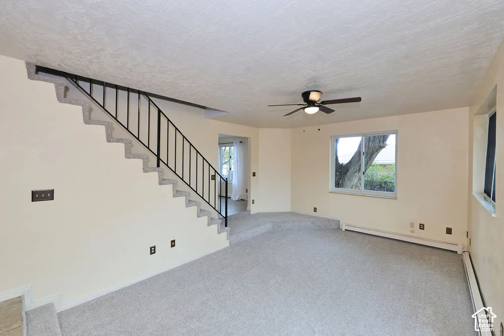 Carpeted interior featuring a tiered floor level, a built-in staircase with a metal railing, and a ceiling fan with integrated lighting
