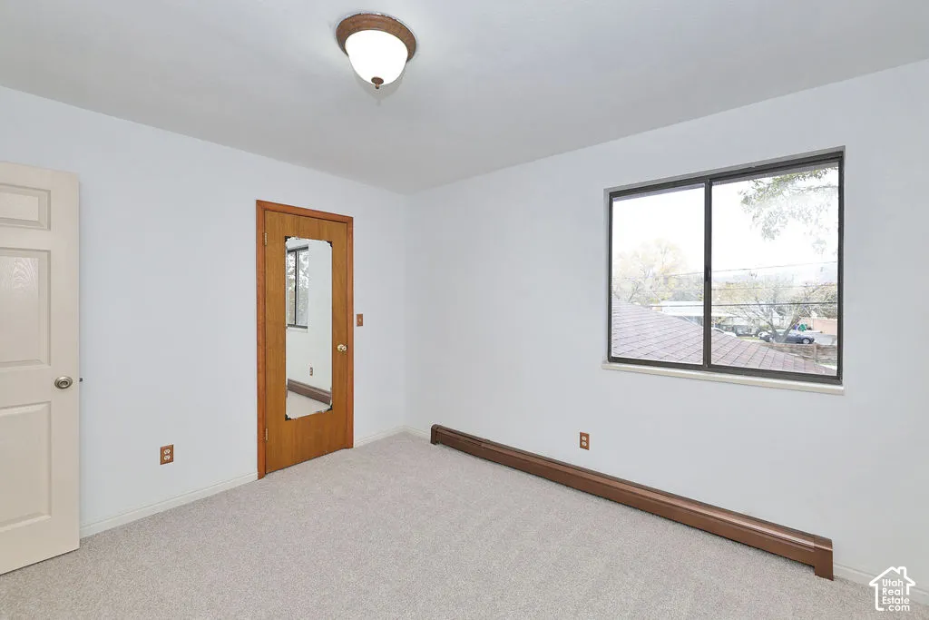 Interior room featuring neutral-toned carpeting, a sliding window with a horizontal frame, a wood-finish door with an inset mirror, and a semi-flush mount dome ceiling light