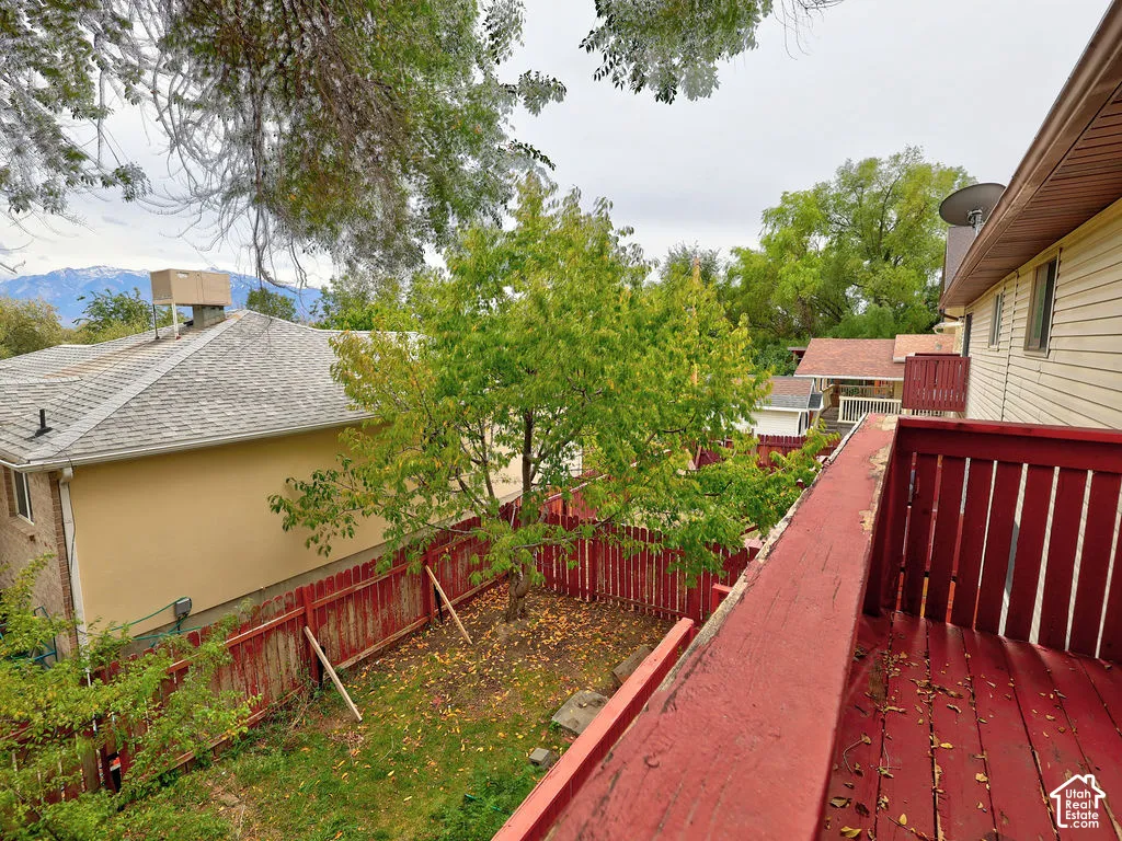 Elevated deck featuring painted wood railings, overlooking a fenced backyard with mature trees and mountain scenery