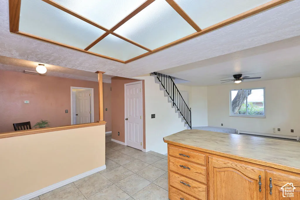 Grid-pattern recessed lighting, tile flooring, built-in wooden cabinetry with a matte countertop, and a staircase with a metal railing