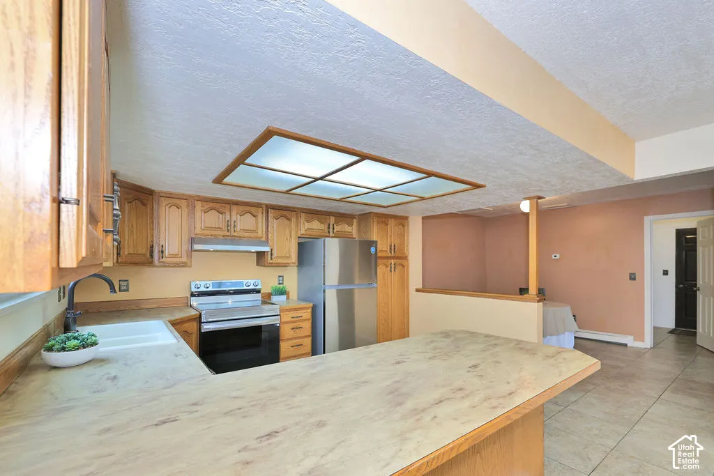 Kitchen featuring wood cabinetry, laminate countertops, stainless steel appliances, tiled flooring, and a recessed ceiling light fixture