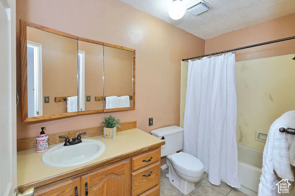 Bathroom featuring wood-frame triple-door medicine cabinet, wood vanity with solid-surface countertop, integrated basin, and tiled flooring