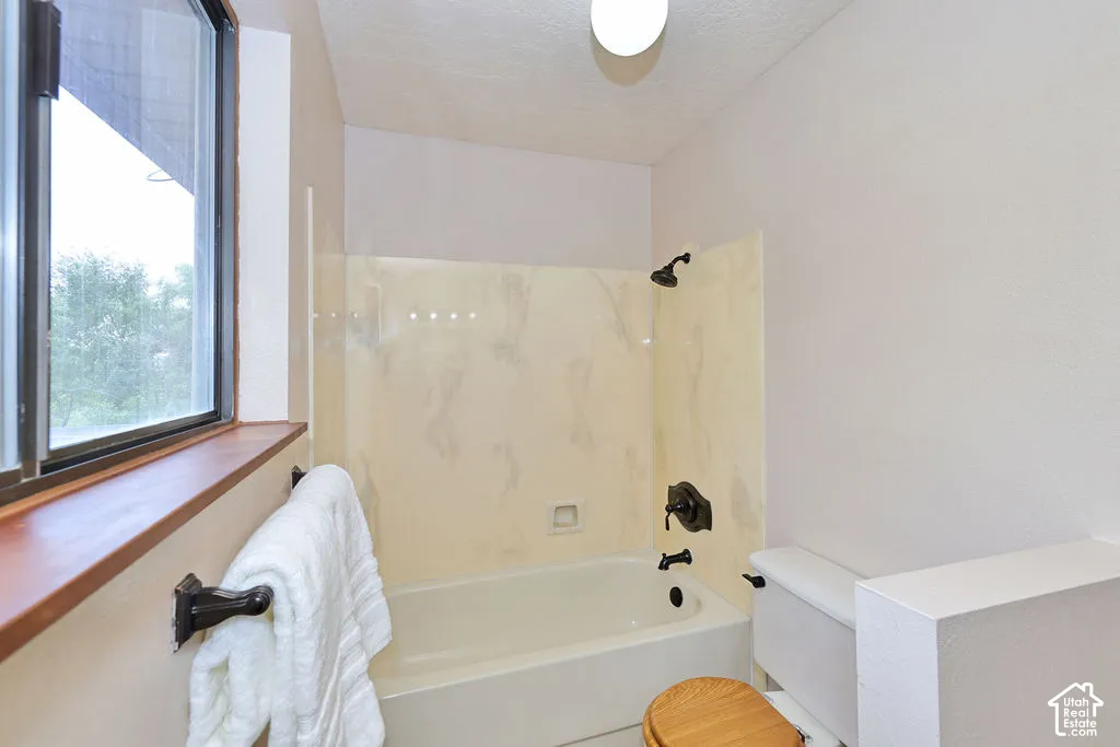 Bathroom featuring a porcelain tub and shower combination with stone-finish surround, dark bronze fixtures, and a natural wood window sill