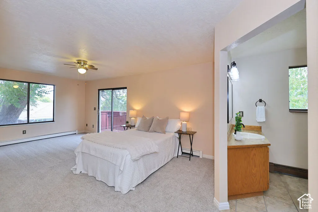 Neutral-toned interior space featuring carpeted flooring, a ceiling fan with integrated lighting, sliding glass door access to an exterior deck, and a vanity area with a stone-top sink and wall-mounted light fixture