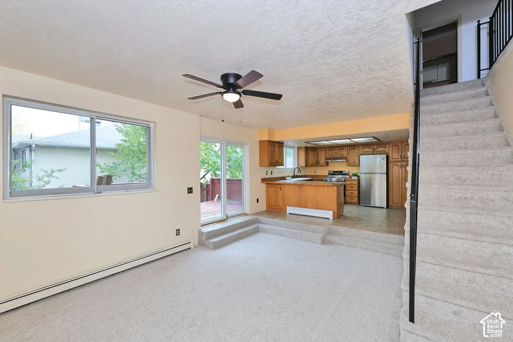 Living space featuring wall-to-wall carpeting, a ceiling fan, sliding glass door, kitchen with wood cabinetry, and a carpeted staircase with a metal handrail