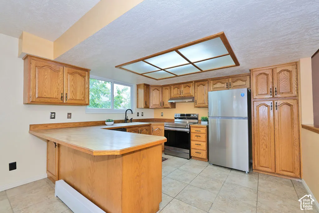 Kitchen featuring wood cabinetry, stainless steel appliances, tile flooring, a peninsula with ample counter space, and integrated recessed lighting