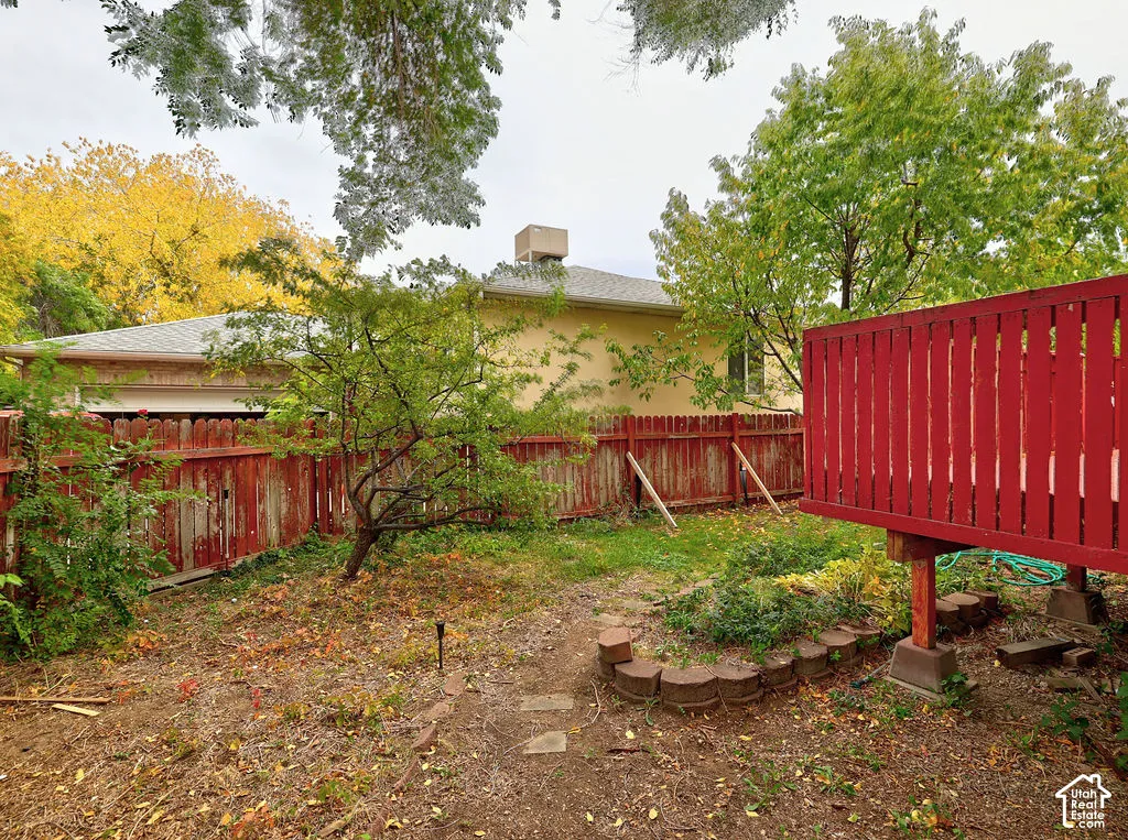 Backyard featuring an elevated wood deck, partial wood perimeter fencing, and a curved stone-block garden bed