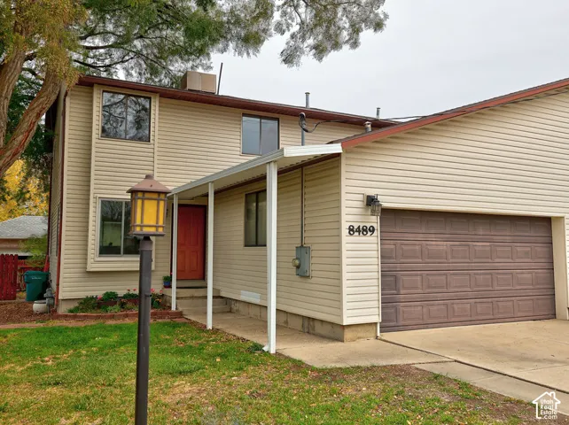 Two-story exterior featuring light-toned vinyl siding, an attached two-car garage with a sectional door, a covered porch entrance, and a concrete driveway