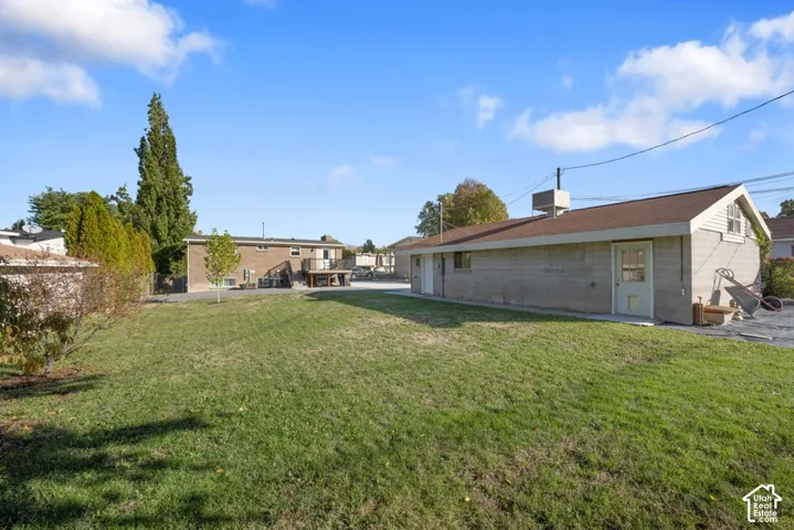 Exterior grounds featuring a grass lawn, mature trees, a detached masonry structure, and a wood-decked patio