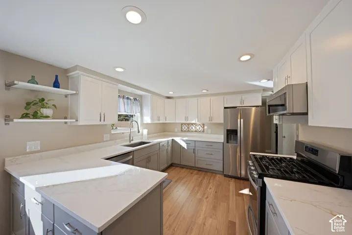 Kitchen featuring two-tone cabinetry, stone-finish countertops, stainless steel appliances, open shelving, and wood-finish flooring