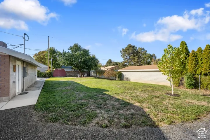Expansive backyard featuring a sprawling lawn, masonry perimeter wall, mature trees, and a detached storage structure