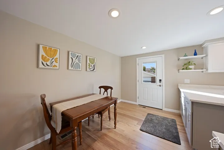 Wood-finish flooring, neutral wall tones, recessed lighting, white cabinetry with stone-surface countertops, and wall-mounted shelving