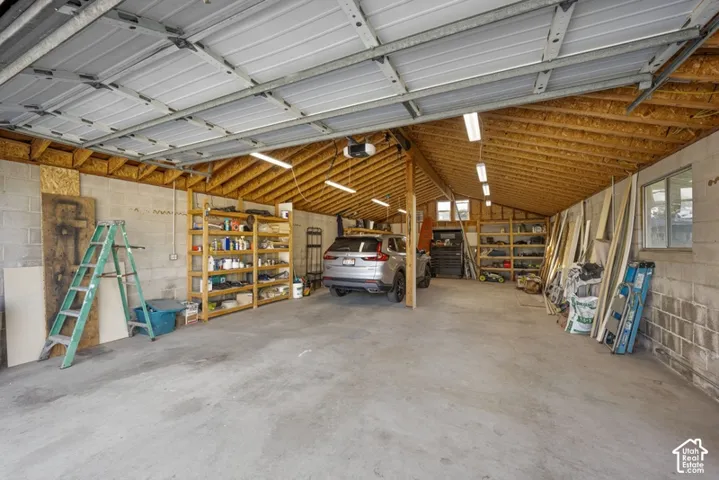 Spacious garage featuring concrete flooring, exposed wood-truss ceiling, overhead lighting, and concrete masonry walls