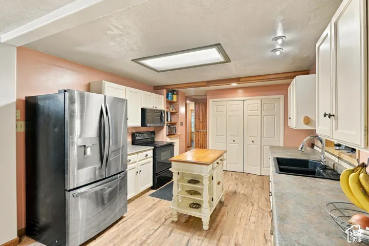 Kitchen featuring wood-finish flooring, stainless steel refrigerator, black undermount sink with gooseneck faucet, light-toned cabinetry, and recessed lighting