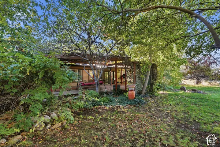 Expansive backyard featuring a sprawling lawn, mature trees, tiered rock garden, and a wooden pergola covering the deck
