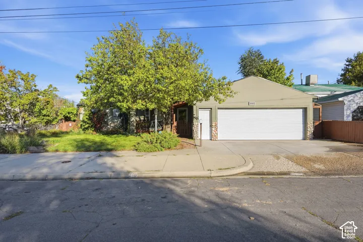 Single-story exterior featuring a two-car garage, stone-accented facade, concrete driveway, and mature landscaping