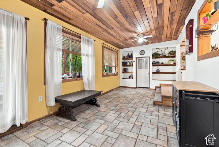 Tongue-and-groove wood-plank ceiling, natural stone-tile flooring, built-in wall shelving, and multiple windows with wood-trim casings