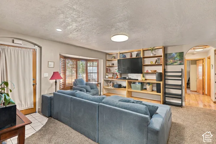 Living space featuring built-in wooden shelving, a multi-pane bay window with plantation-style shutters, arched doorways, and recessed lighting