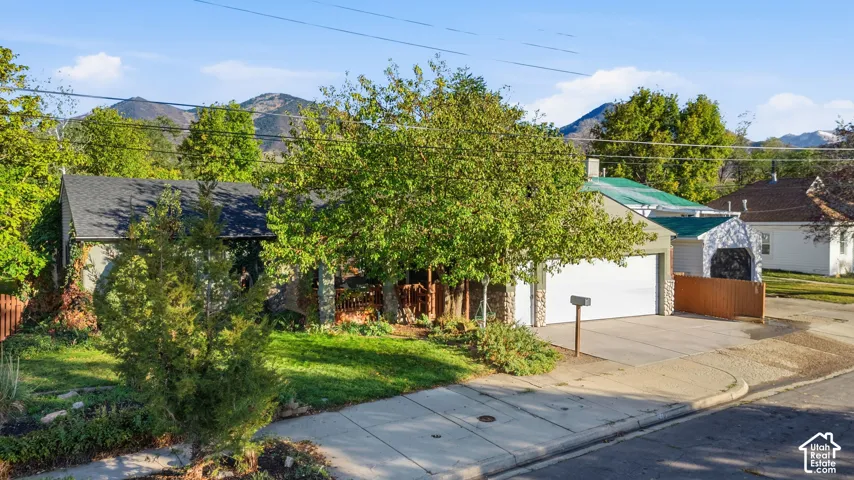 Single-story exterior featuring a two-car garage, stone masonry accents, covered porch, and mature trees against a mountain backdrop
