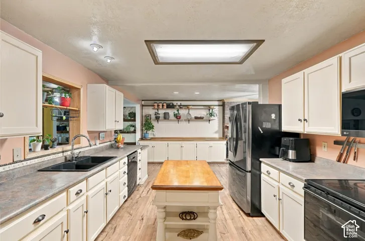 Kitchen featuring white cabinetry, wood-finish flooring, a central island with a wood countertop, matte black dual-basin sink, and integrated shelving
