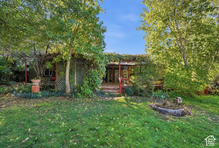 Expansive backyard featuring a mature canopy of trees, wooden deck with pergola, trellis privacy screen, and stone fire pit