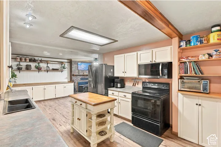 Kitchen featuring white cabinetry, wood-finish flooring, a wood-topped kitchen island, built-in open shelving, and a brick accent wall