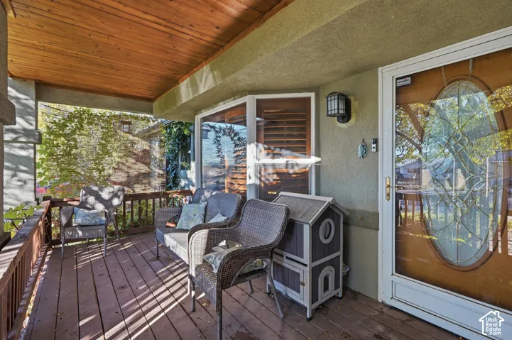 Covered front porch featuring wood-plank ceiling, wood-finish decking, and an entry door with oval decorative glass insert