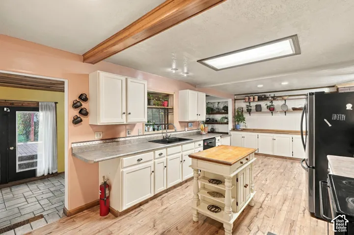 Kitchen featuring white cabinetry, wood-finish flooring, exposed ceiling beams, a central island with a wood countertop, and a recessed skylight
