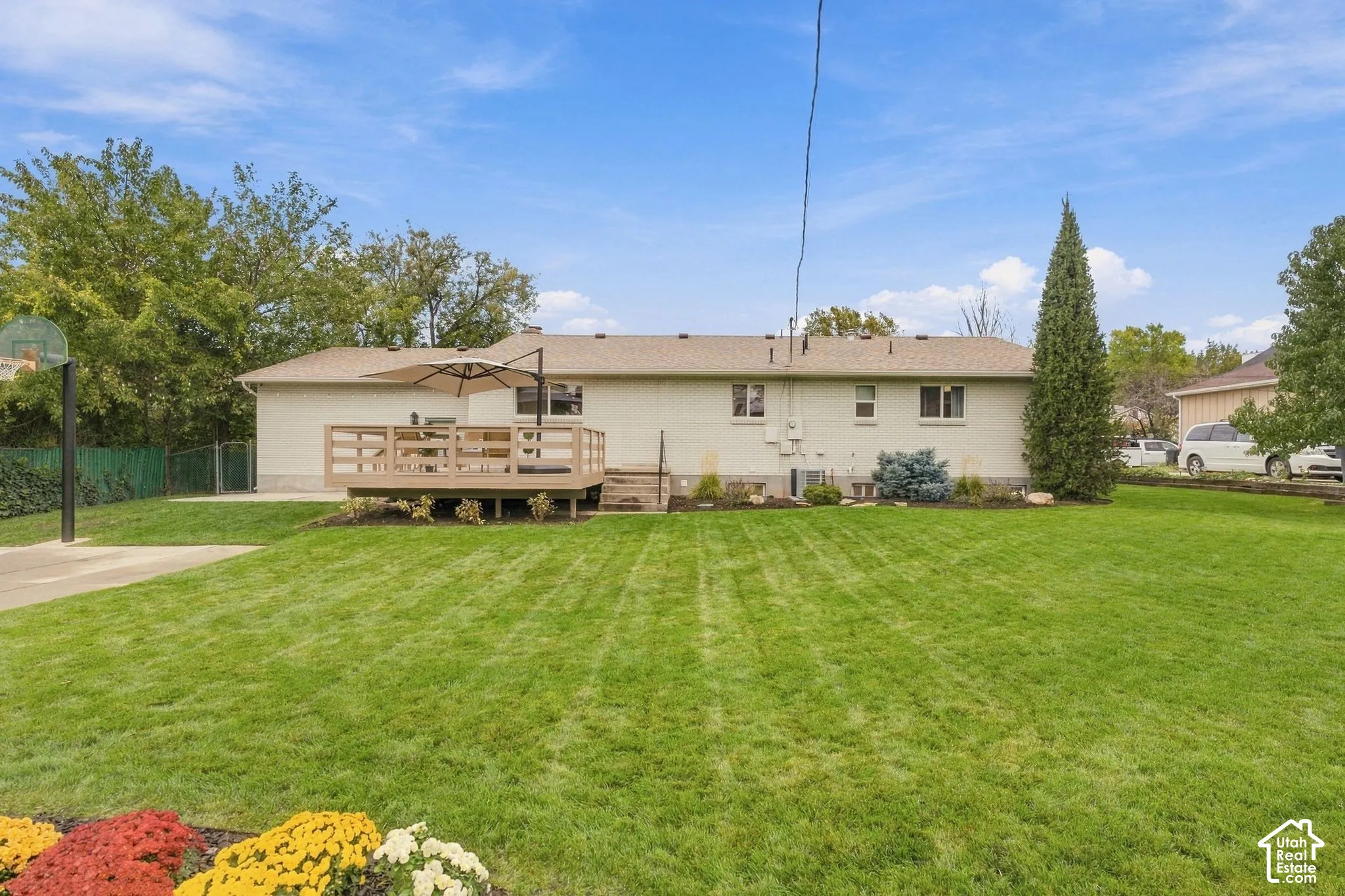 Rear exterior featuring a brick facade, raised wood-finish deck, concrete driveway, and expansive lawn with mature landscaping