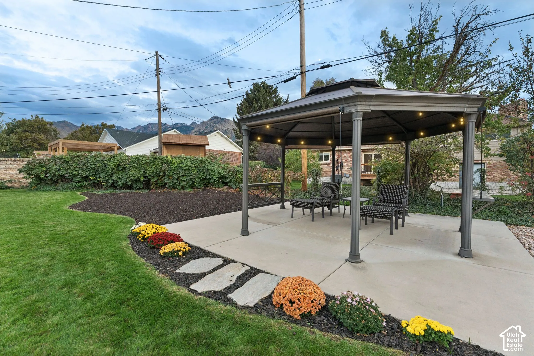 Backyard featuring a concrete patio, metal-frame gazebo, manicured lawn, stone pathway, and mountain backdrop