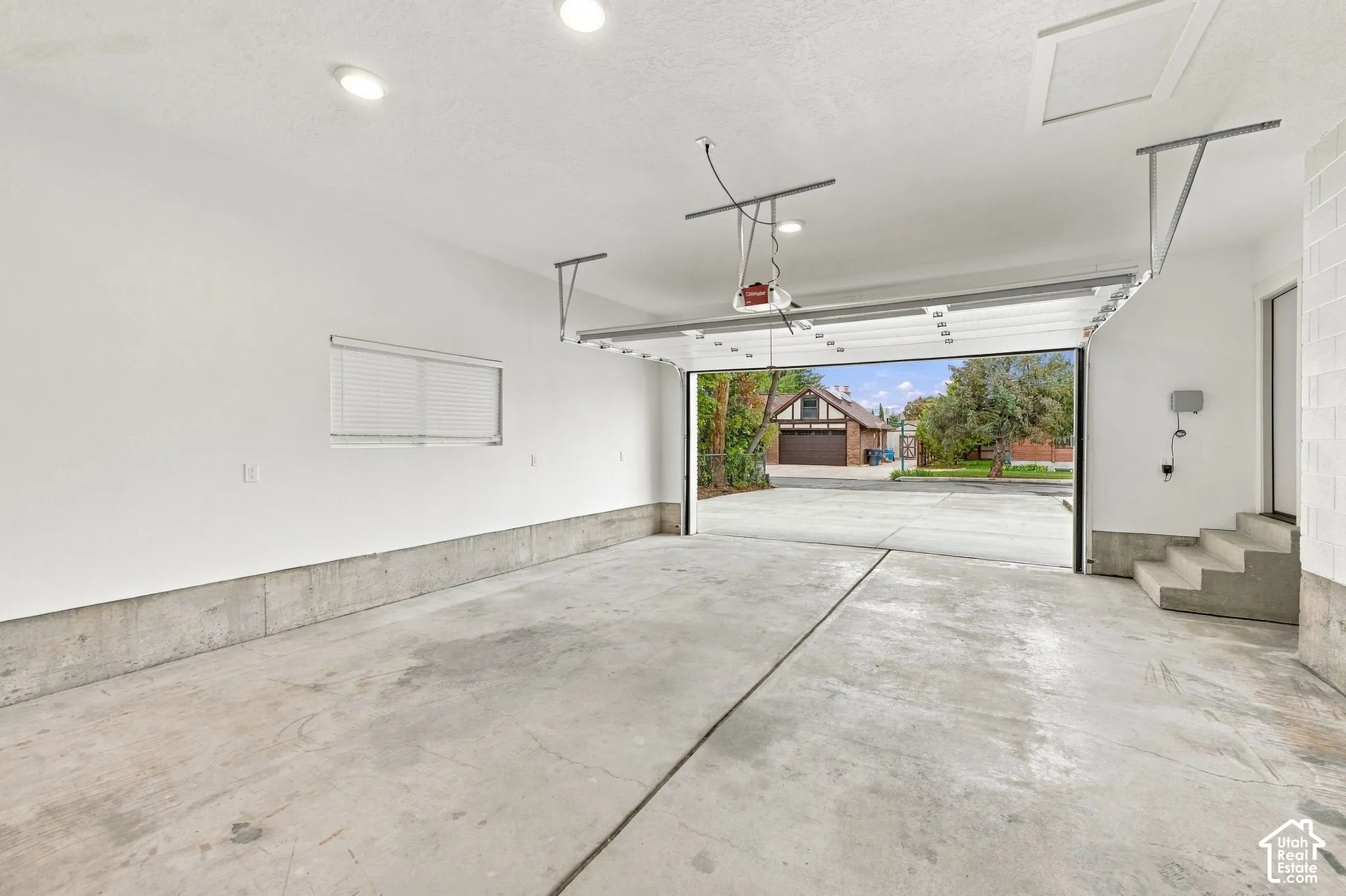 Spacious garage featuring polished concrete flooring, overhead storage systems, and a wide roll-up door opening to natural light and direct driveway access