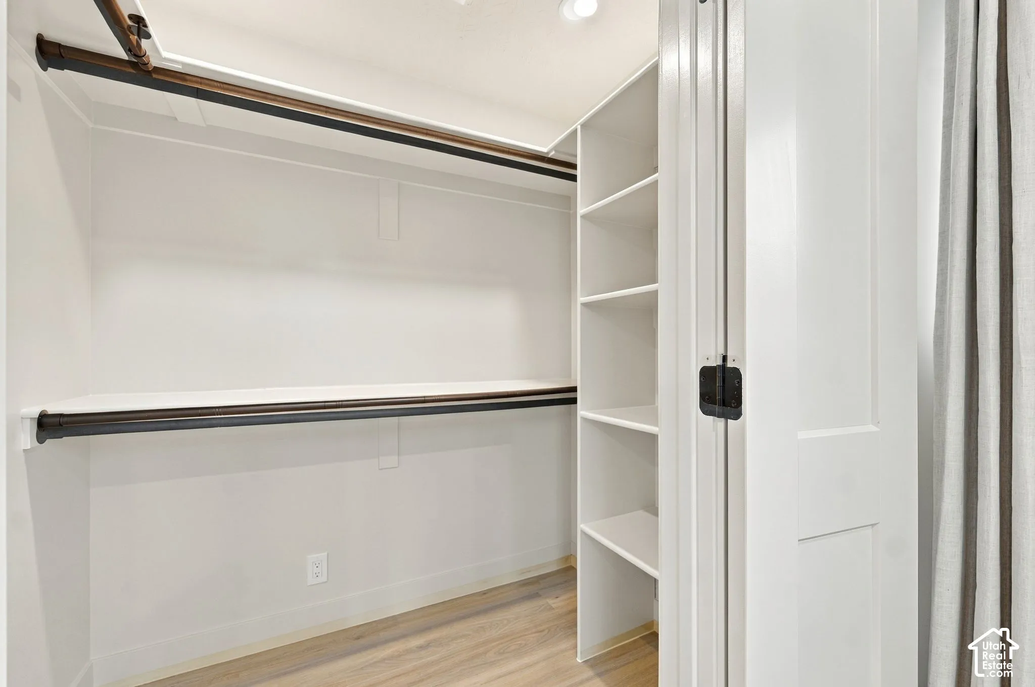Spacious walk-in closet featuring dual black metal hanging rods, built-in shelving along the perimeter, wood-finish flooring, and bright overhead lighting