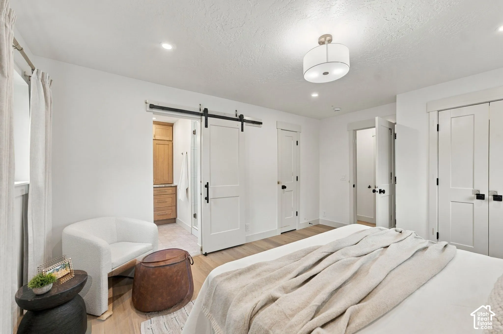 Room featuring wood-finish flooring, a white sliding barn door with matte black hardware, recessed lighting, and a multi-light drum pendant fixture