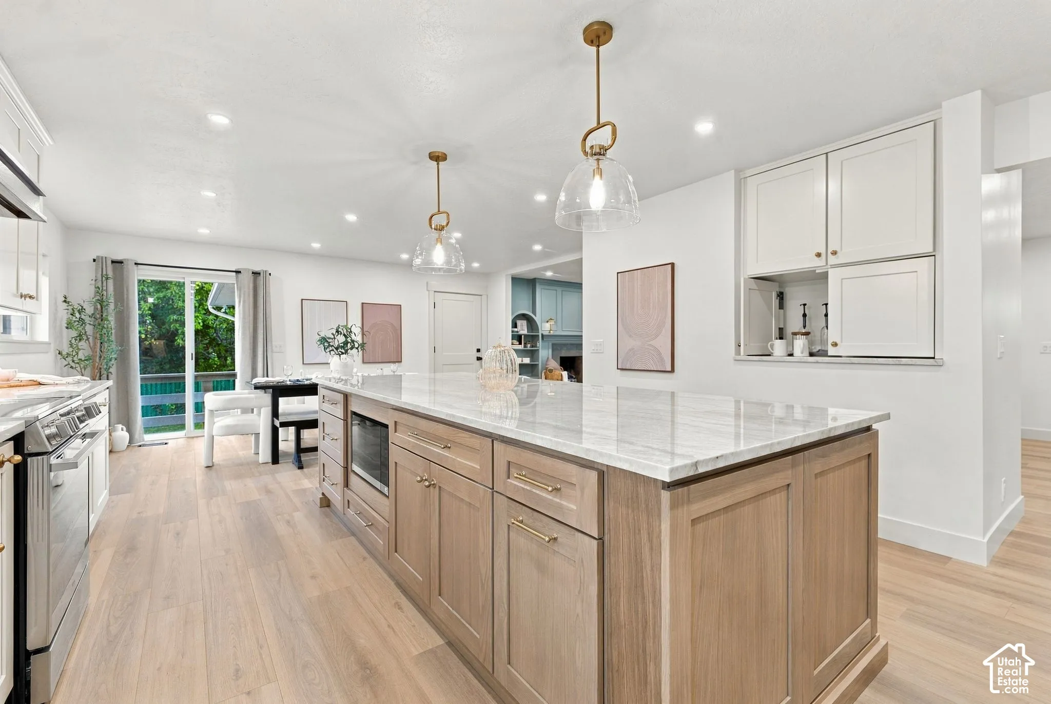 Chef's kitchen featuring a wood-finish island with white quartz countertops, stainless steel appliances, white cabinetry with integrated hardware, pendant lighting, and wide-plank wood-finish flooring throughout