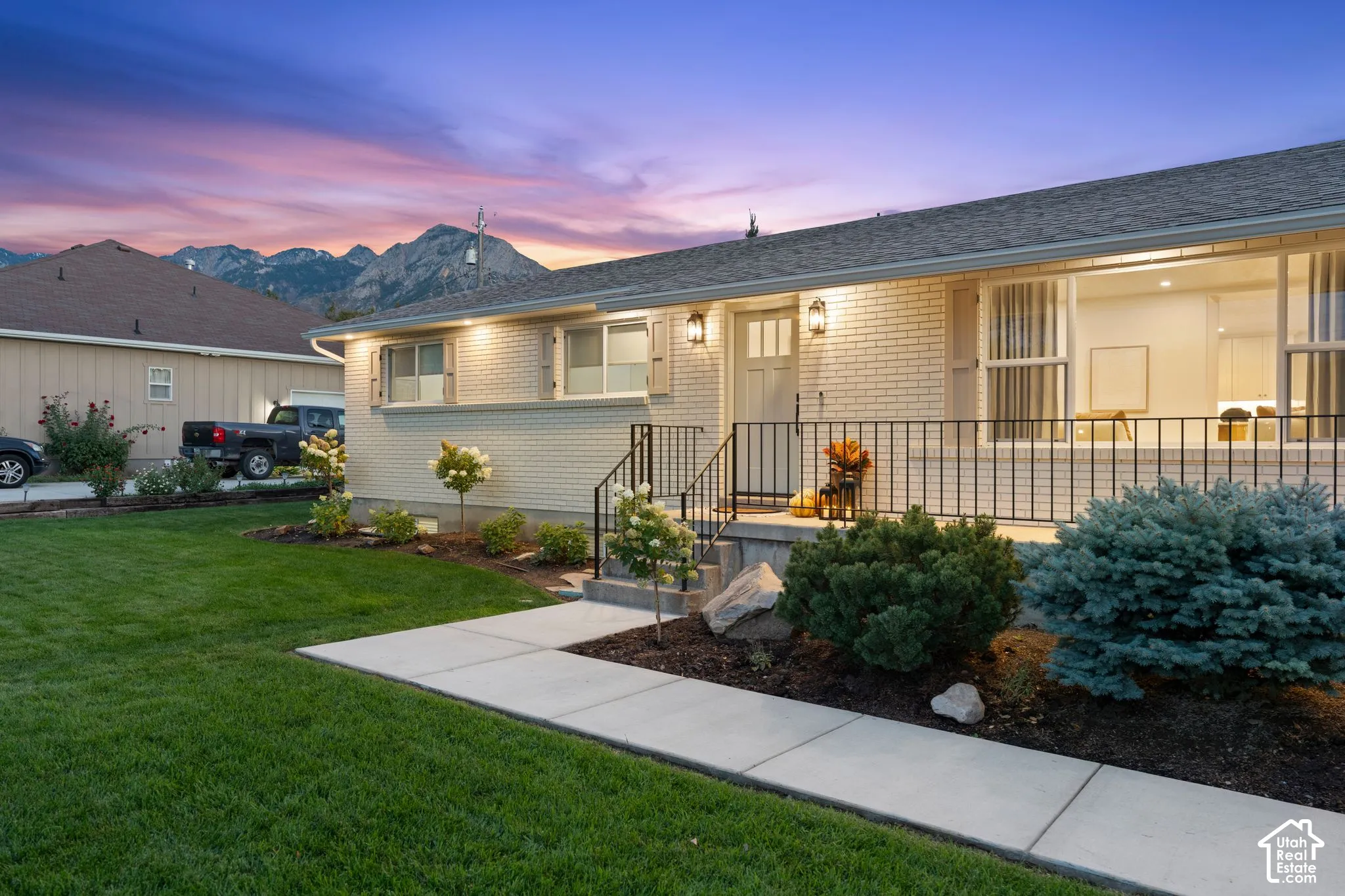 Brick exterior featuring a concrete walkway, black metal railing, and mountain backdrop